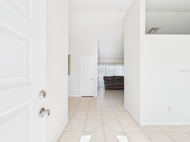 corridor with vaulted ceiling, light tile patterned flooring, visible vents, and baseboards