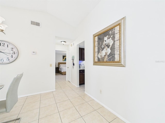 hall with vaulted ceiling, light tile patterned floors, visible vents, and baseboards