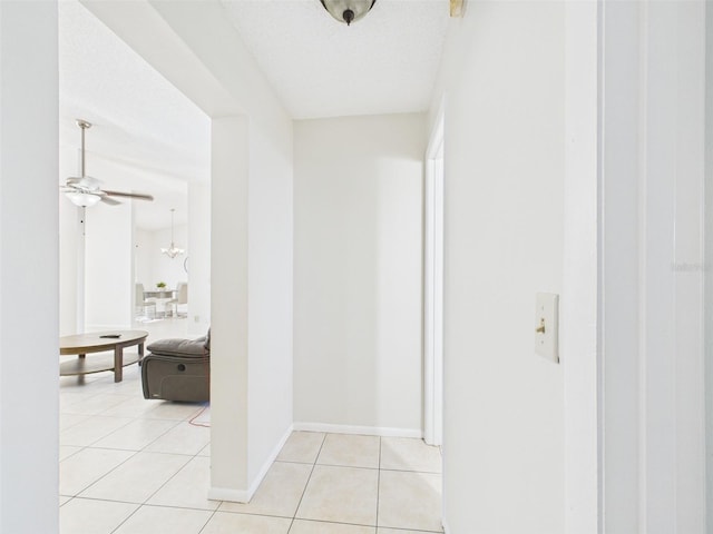 hallway with light tile patterned floors, baseboards, and a textured ceiling