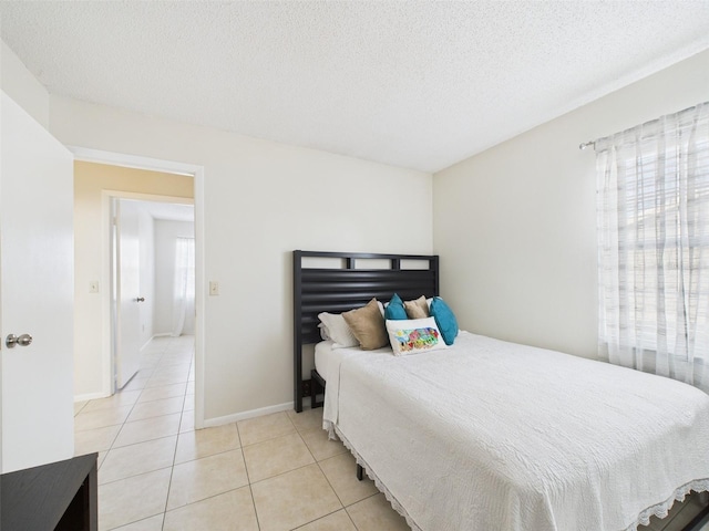 bedroom featuring multiple windows, baseboards, a textured ceiling, and light tile patterned flooring