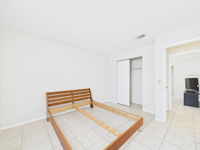 bedroom featuring light tile patterned floors, baseboards, visible vents, and a closet