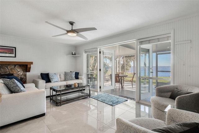 living area with a water view, ornamental molding, a ceiling fan, and a stone fireplace