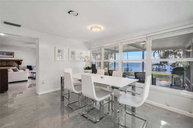 dining room featuring a stone fireplace, a water view, visible vents, and baseboards