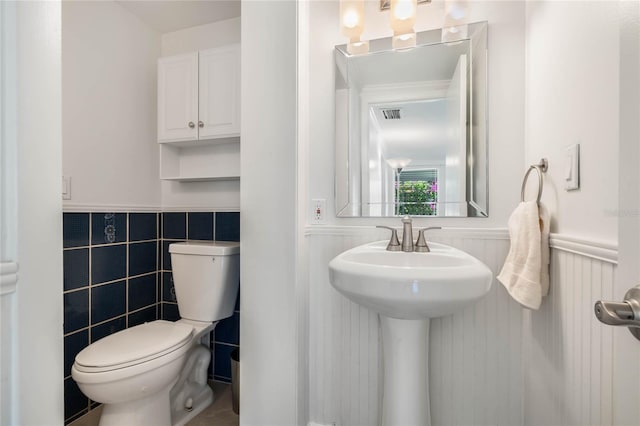 half bath featuring a wainscoted wall, visible vents, and toilet