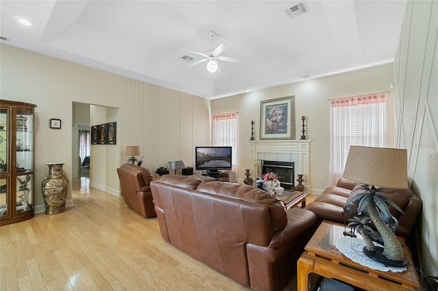 living area featuring a tray ceiling, a tile fireplace, visible vents, and light wood-style floors