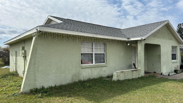 view of home's exterior with a yard, roof with shingles, and stucco siding