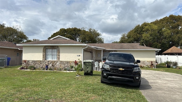 ranch-style home with concrete driveway, stone siding, stucco siding, fence, and a front yard