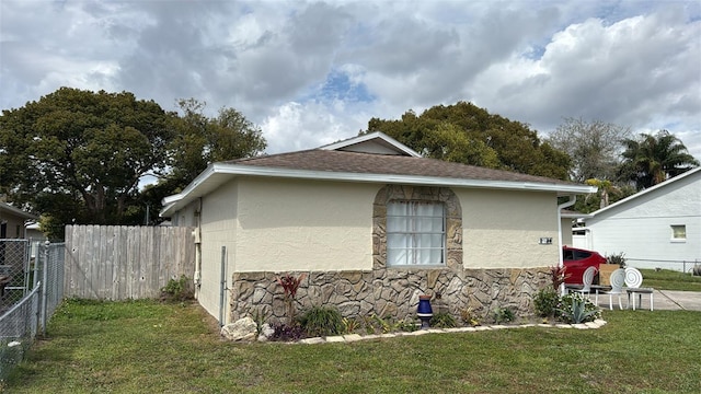 view of property exterior with stone siding, a yard, fence, and stucco siding