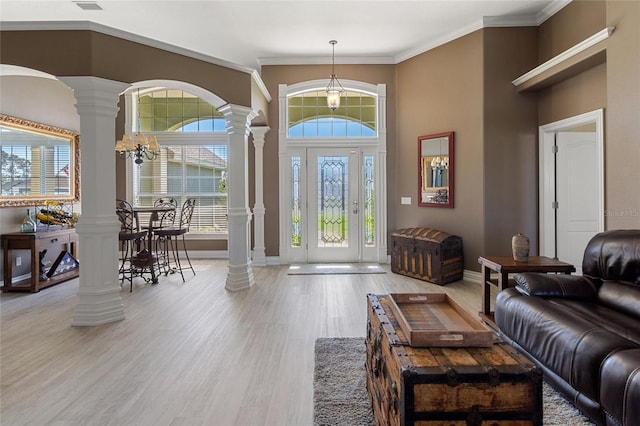 entryway featuring a chandelier, wood finished floors, baseboards, decorative columns, and crown molding