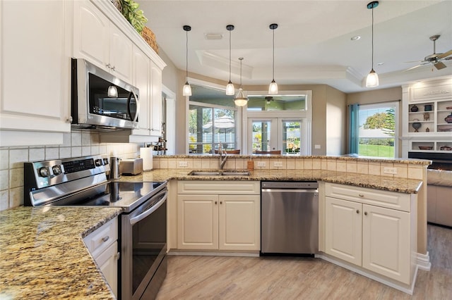 kitchen featuring a tray ceiling, pendant lighting, stainless steel appliances, white cabinetry, and a peninsula