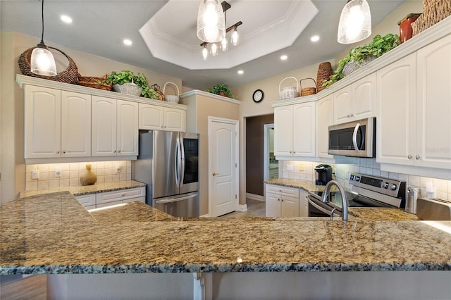 kitchen featuring stainless steel appliances, a peninsula, a raised ceiling, and pendant lighting