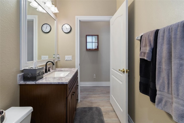 bathroom featuring toilet, baseboards, wood finished floors, and vanity