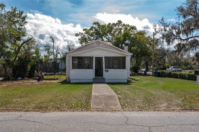 bungalow-style home with a trampoline, a chimney, a sunroom, and a front yard