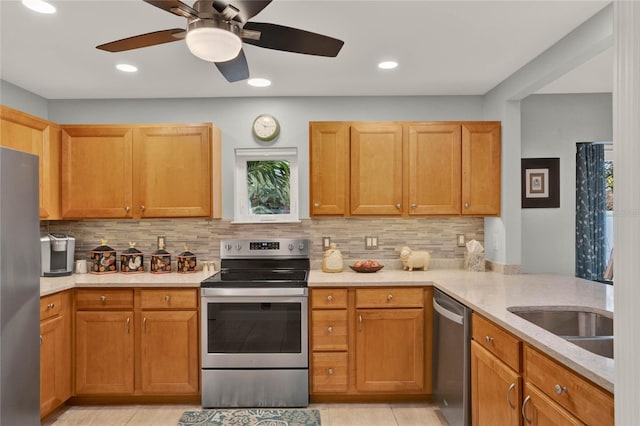 kitchen with tasteful backsplash, appliances with stainless steel finishes, a peninsula, light stone countertops, and a sink