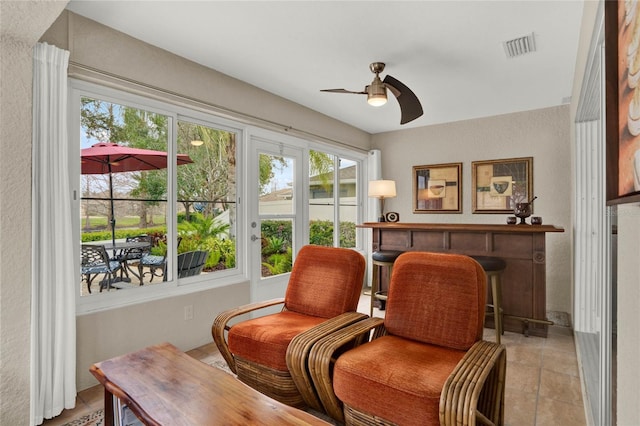 living area featuring a textured wall, visible vents, and a ceiling fan