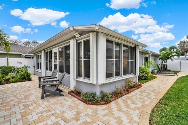 view of property exterior with a sunroom, fence, and a patio