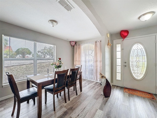 dining area with baseboards, visible vents, arched walkways, a textured ceiling, and light wood-style floors