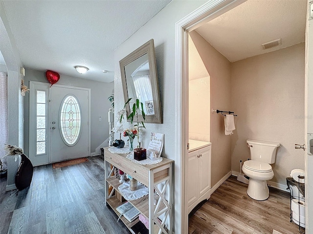 foyer entrance featuring visible vents, a textured ceiling, baseboards, and wood finished floors