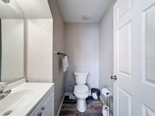 half bathroom with baseboards, visible vents, toilet, wood finished floors, and vanity