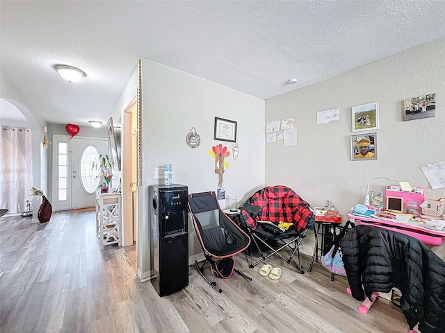 recreation room featuring baseboards, a textured ceiling, arched walkways, and wood finished floors