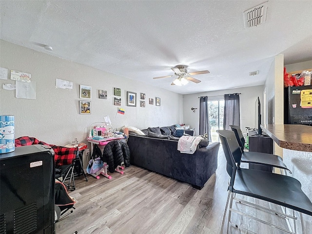 living area with a textured ceiling, ceiling fan, wood finished floors, and visible vents