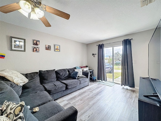 living area featuring a textured ceiling, ceiling fan, visible vents, and light wood-style floors