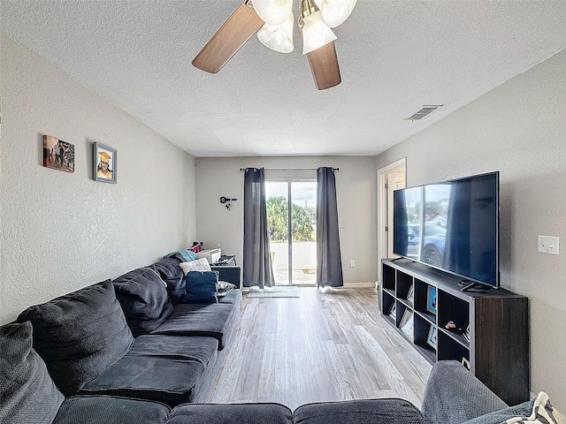 living room with light wood-style floors, visible vents, a textured ceiling, and a textured wall