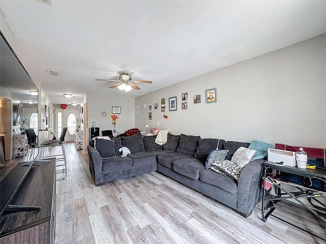 living area featuring light wood-type flooring, ceiling fan, visible vents, and a textured ceiling