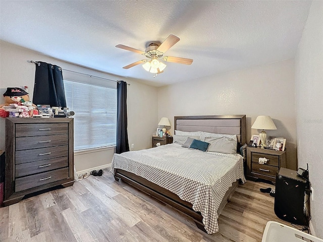 bedroom featuring light wood-type flooring, baseboards, a ceiling fan, and a textured ceiling