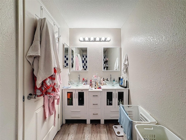 full bathroom with double vanity, a textured wall, a sink, a textured ceiling, and wood finished floors