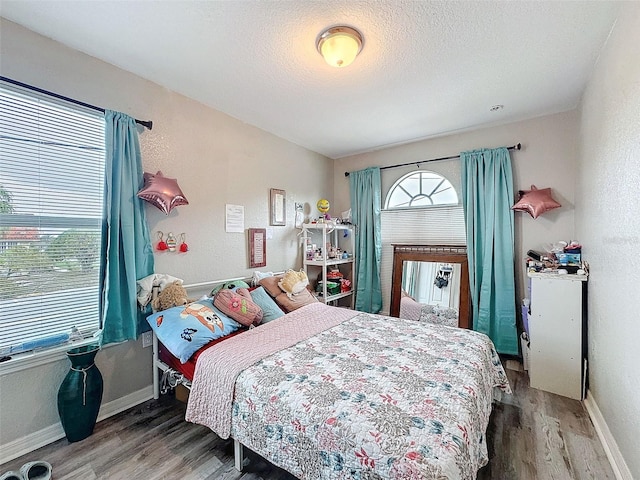 bedroom with a textured ceiling, multiple windows, and wood finished floors