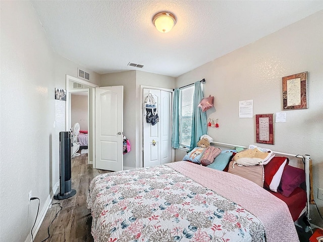 bedroom featuring a closet, visible vents, a textured ceiling, and wood finished floors