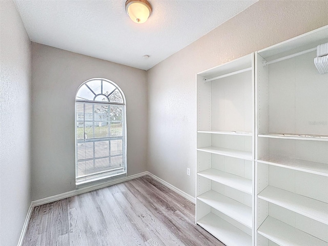 empty room with a textured ceiling, baseboards, and light wood-style floors