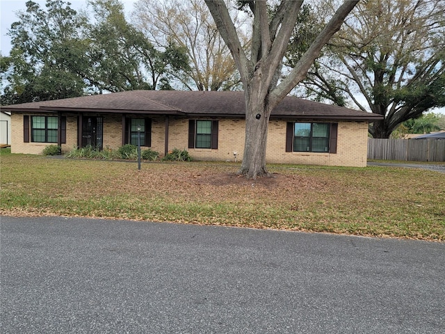 ranch-style home featuring brick siding, a front yard, and fence