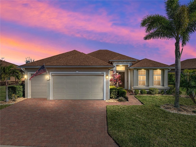 view of front of property featuring a front yard, decorative driveway, an attached garage, and stucco siding