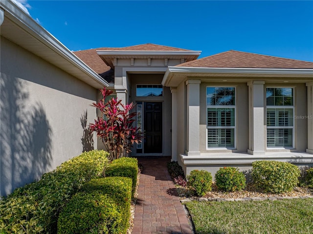 view of exterior entry with a shingled roof and stucco siding