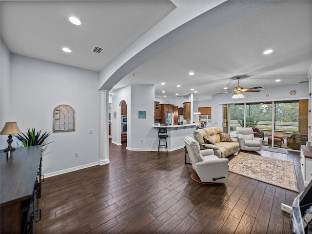 living area featuring arched walkways, ceiling fan, dark wood-type flooring, baseboards, and decorative columns