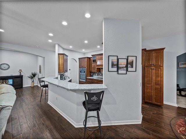 kitchen with a peninsula, light stone counters, dark wood-style flooring, and a kitchen bar