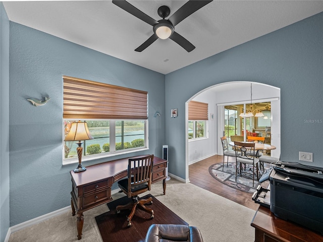 carpeted office featuring baseboards, arched walkways, a textured wall, ceiling fan, and wood finished floors