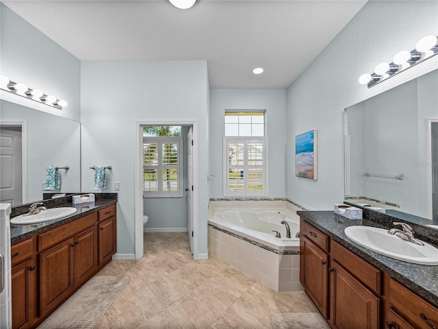 full bath with a garden tub, two vanities, a sink, and toilet