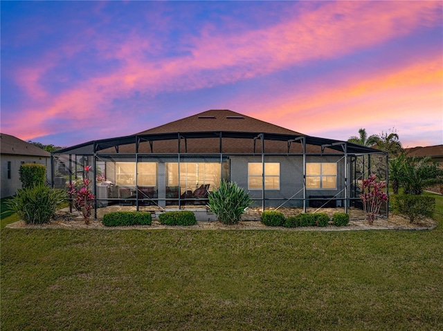 back of house at dusk with a lanai, a lawn, and stucco siding