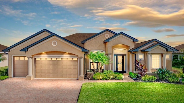 ranch-style house featuring a garage, a yard, decorative driveway, and stucco siding