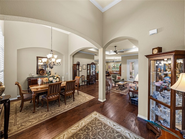 dining space featuring arched walkways, ceiling fan with notable chandelier, a towering ceiling, dark wood finished floors, and crown molding