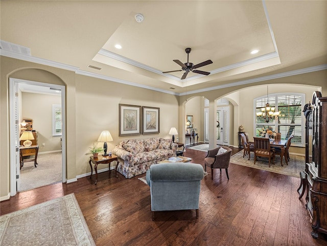 living area featuring dark wood-type flooring, a tray ceiling, and arched walkways