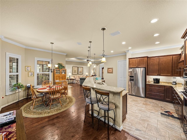 kitchen featuring visible vents, light stone counters, crown molding, pendant lighting, and high end fridge