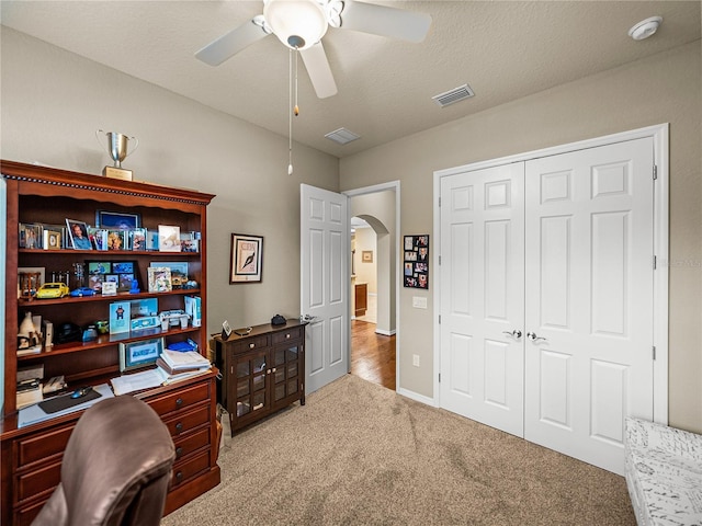 office space featuring carpet floors, arched walkways, visible vents, ceiling fan, and a textured ceiling