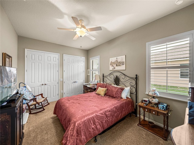 carpeted bedroom featuring a ceiling fan, multiple windows, baseboards, and two closets