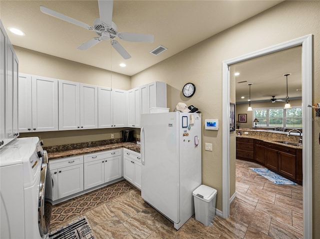 kitchen with ceiling fan, a sink, washer and dryer, freestanding refrigerator, and dark stone countertops