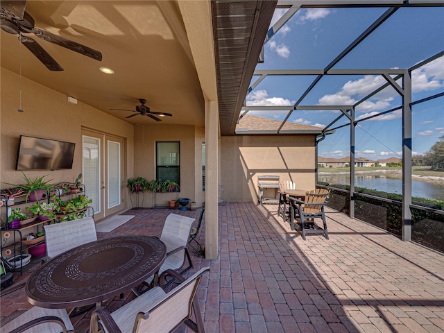 view of patio featuring a ceiling fan, glass enclosure, a water view, outdoor dining area, and french doors