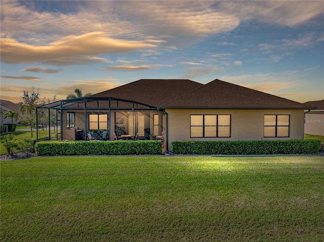 back of property at dusk with a lawn, a lanai, and stucco siding